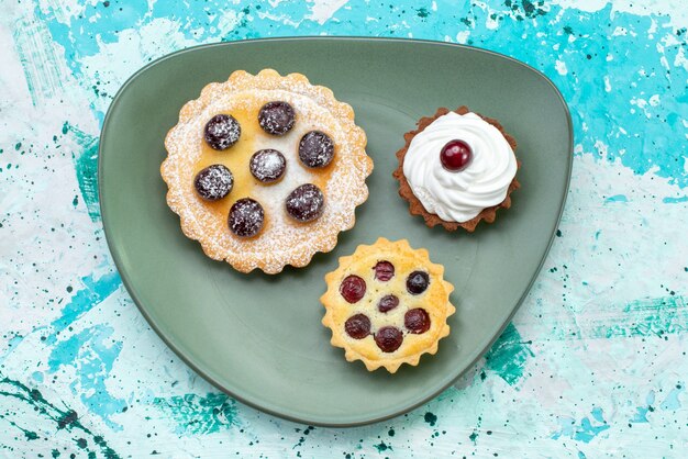 Vista de cima pequenos bolos saborosos com açúcar em pó creme de frutas dentro do prato azul mesa bolo creme fruta doce chá