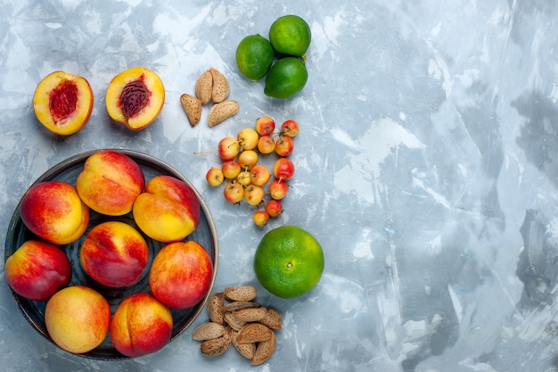 Vista de cima, pêssegos frescos, deliciosas frutas de verão com tangerinas na mesa branca