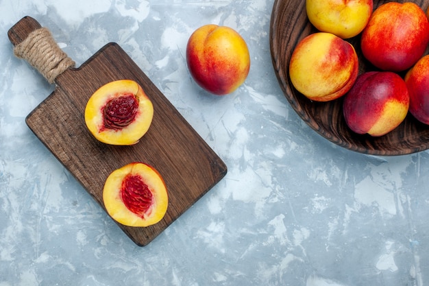 Foto grátis vista de cima pêssegos frescos e frutas saborosas em um prato marrom sobre a mesa branca clara