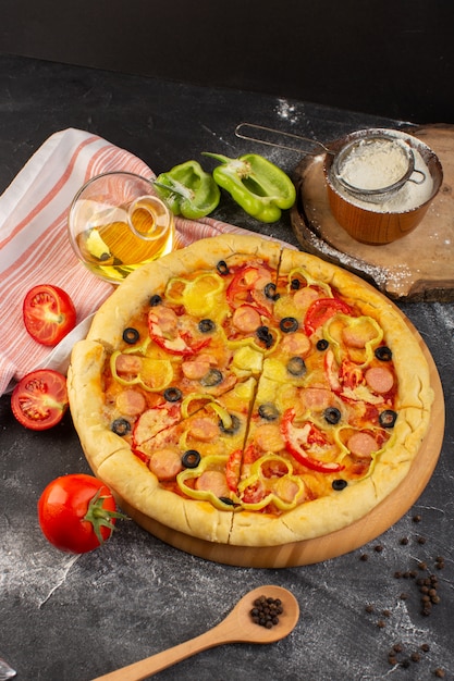 Vista de cima, pizza saborosa de queijo com tomates vermelhos, azeitonas pretas e salsichas na mesa escura com azeite e tomates frescos, massa italiana fast-food