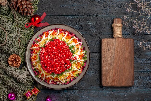Vista de cima prato apetitoso prato apetitoso de Natal com romã ao lado dos galhos das árvores e tábua de madeira