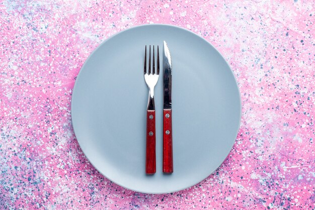 Vista de cima prato vazio de cor azul com garfo e faca na parede rosa brilhante prato de fotos coloridas talheres de comida