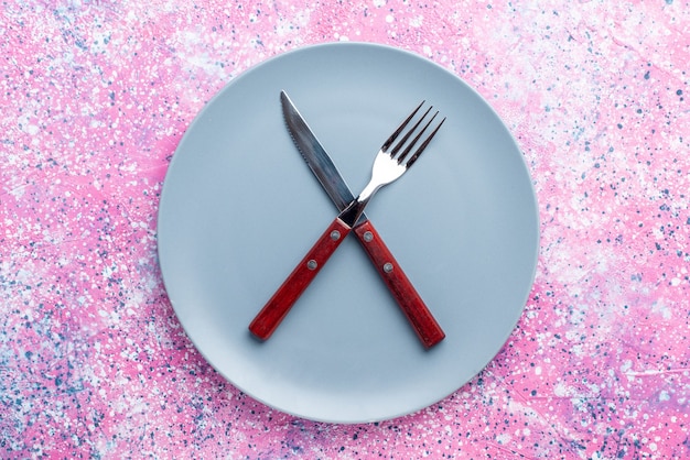 Vista de cima prato vazio de cor azul com garfo e faca na parede rosa prato de foto colorida talheres de comida