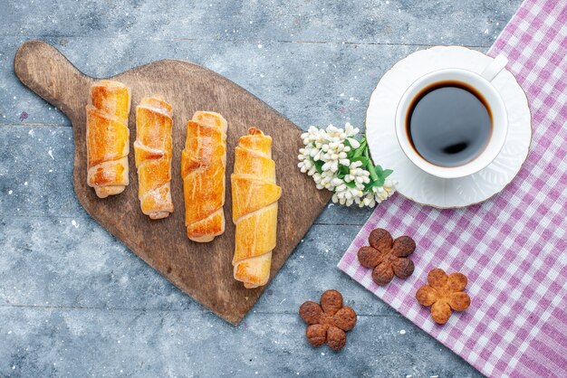 Vista de cima, pulseiras deliciosas e doces com recheio e biscoitos de café na mesa de madeira cinza.