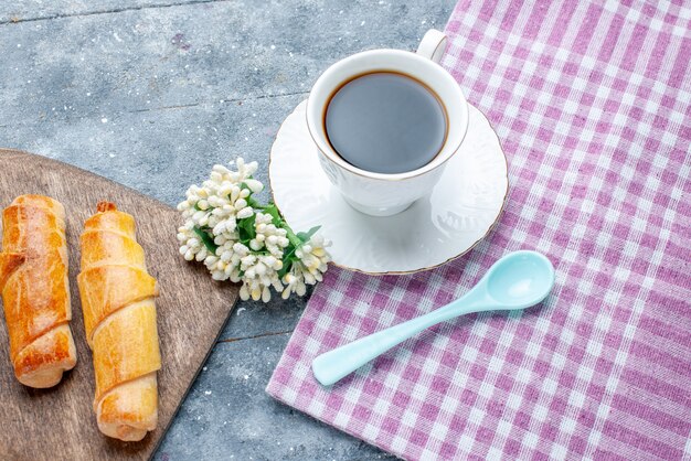 Vista de cima, pulseiras deliciosas e doces com recheio e uma xícara de café sobre a mesa cinza.