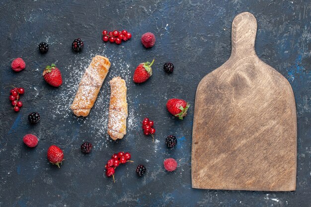 Vista de cima, pulseiras deliciosas e doces com recheio gostoso, assadas com frutas e morangos na mesa escura, assar bolo, biscoito, sobremesa