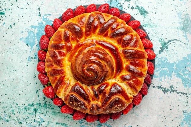 Vista de cima redonda deliciosa torta com morangos vermelhos em uma superfície azul clara