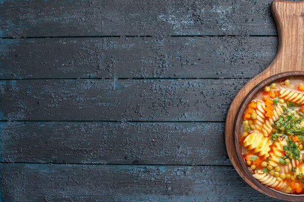 Foto grátis vista de cima saborosa sopa de macarrão com macarrão espiral italiano com verduras em um prato azul escuro de cozinha de mesa