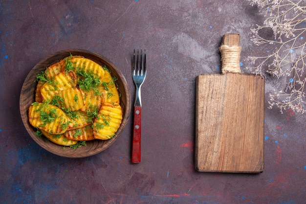 Vista de cima saborosas batatas cozidas com verduras dentro de um prato marrom em um prato de refeição de superfície escura cozinhando batatas cips para o jantar