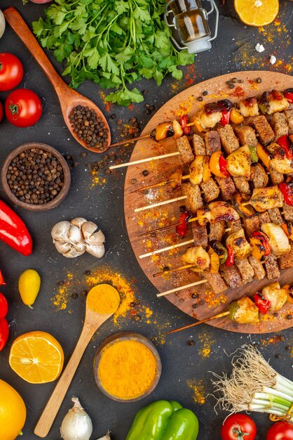 Vista de cima saborosos espetos de frango na tábua de madeira e outros alimentos na mesa