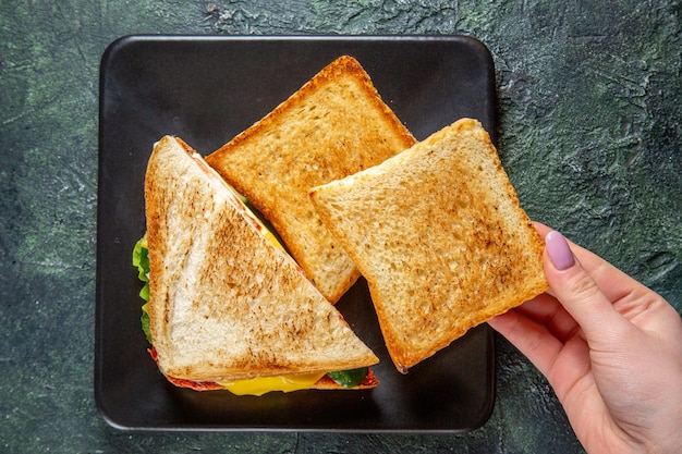 Vista de cima saborosos sanduíches de presunto com torradas dentro do prato em superfície escura