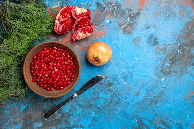 Vista de cima sementes de romã em uma tigela faca de jantar um galho de árvore de pinho de romã cortado em fundo azul espaço livre