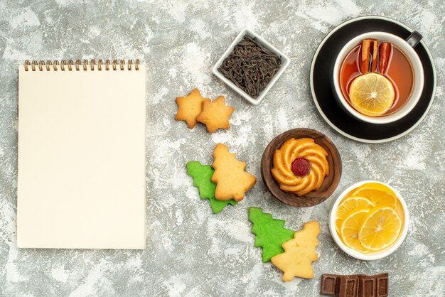 Vista de cima taças de biscoitos de chá de limão e canela com caderno de chocolate e rodelas de limão na superfície cinza