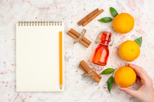 Vista de cima tangerinas frescas em bastões de canela tangerina em garrafa de mão feminina um caderno de lápis na superfície brilhante