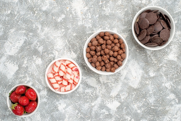 Foto grátis vista de cima tigelas com filas diagonais com doces de morangos e chocolates de cereais no fundo branco-acinzentado