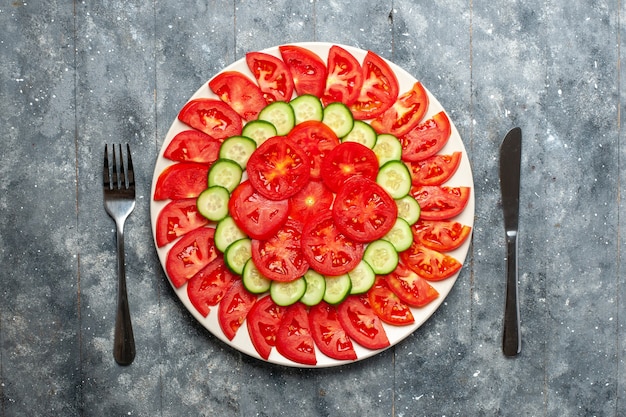 Vista de cima, tomates vermelhos frescos fatiados em fatias de salada na mesa cinza