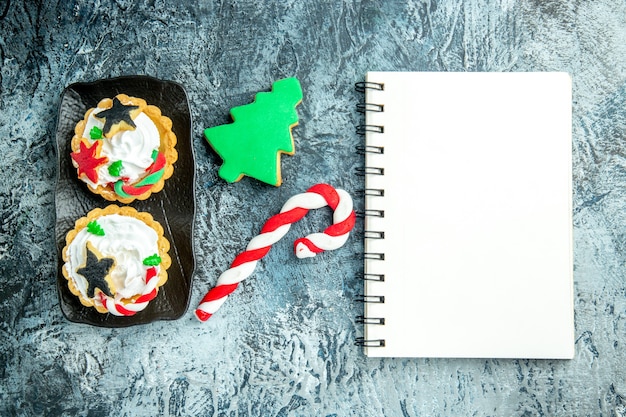 Vista de cima tortas de natal na placa preta doce de natal e bloco de notas de biscoito da árvore de natal na mesa cinza