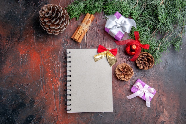 Vista de cima um caderno com um pequeno arco de pinheiro galhos cones, brinquedos de árvore de natal e presentes canela em fundo vermelho escuro