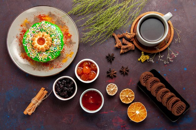 Vista de cima um pequeno bolo delicioso com biscoitos e chá na superfície escura