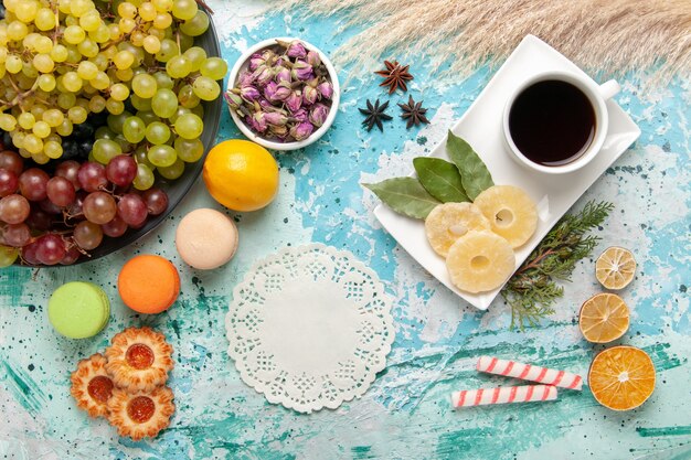 Vista de cima uvas frescas coloridas com uma xícara de chá na superfície azul-clara frutas biscoitos bolo doce bolo assar