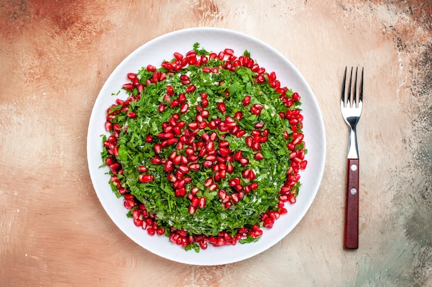 Vista de cima verduras frescas com romãs descascadas em uma mesa clara de cor verde