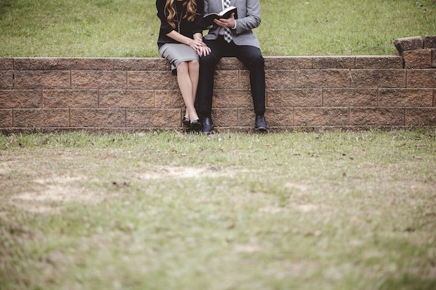 Vista de um casal usando roupas formais, lendo e discutindo um livro enquanto está sentado em um jardim