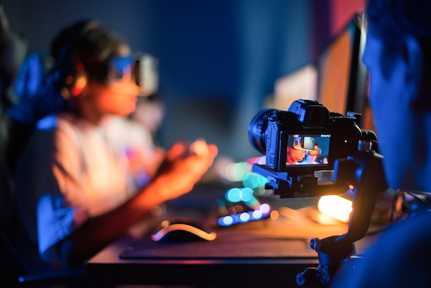 Vista de um fotógrafo profissional filmando adolescentes em fones de ouvido VR jogando videogames em um clube de videogames