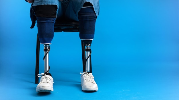 Foto grátis vista de um homem com pernas protéticas e tênis branco sentado em uma cadeira de fundo azul