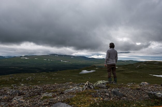 Vista de um homem em uma colina rochosa com nuvens de tempestade