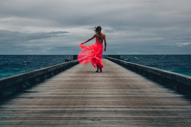 Vista de uma mulher com um vestido longo rosa caminhando no cais em um dia de vento