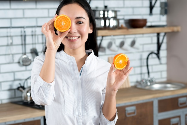 Foto grátis vista dianteira, de, mulher asian, cobertura, dela, um olho, com, fatia laranja, em, cozinha