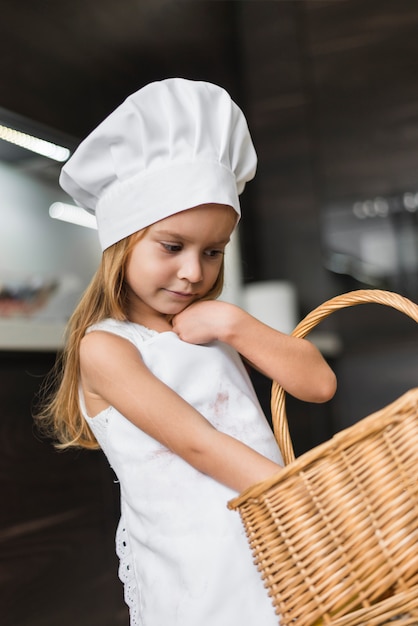 Foto grátis vista dianteira, de, pequeno, cozinheiro, menina, carregar, cesta vime