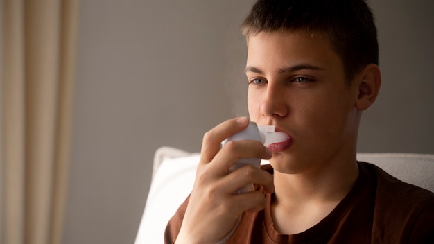 Vista do adolescente usando inalador em casa para problemas de saúde respiratória