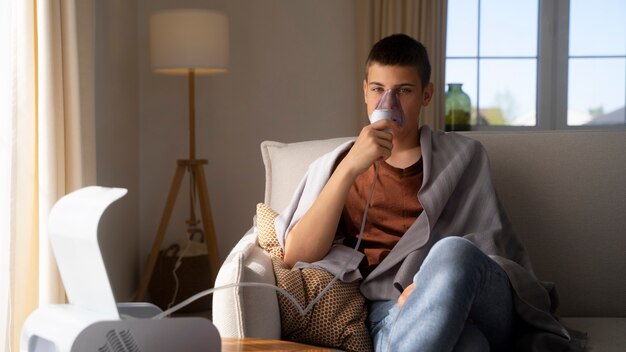 Vista do adolescente usando nebulizador em casa para problemas de saúde respiratória