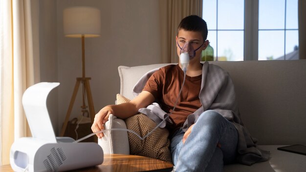 Vista do adolescente usando nebulizador em casa para problemas de saúde respiratória