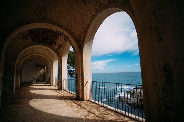 Vista do antigo edifício no oceano ou mar com colunas romanas e ruínas históricas na linha da costa mediterrânea.