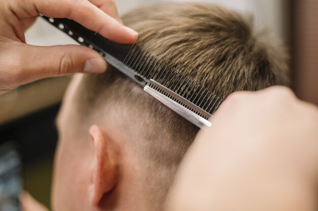 Vista do close-up de cabeleireiro dando um corte de cabelo para um cliente