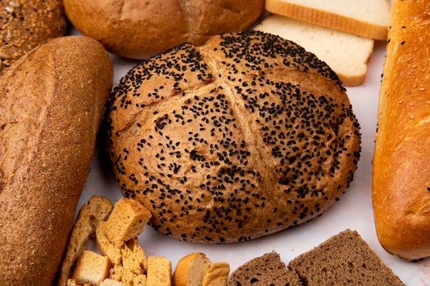 Vista do close-up de espiga de semente de papoula com baguete sem sementes e pedaços de pão e outros pães no fundo branco