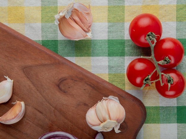 Vista do close-up de legumes como alho na superfície de madeira e tomate na superfície de pano