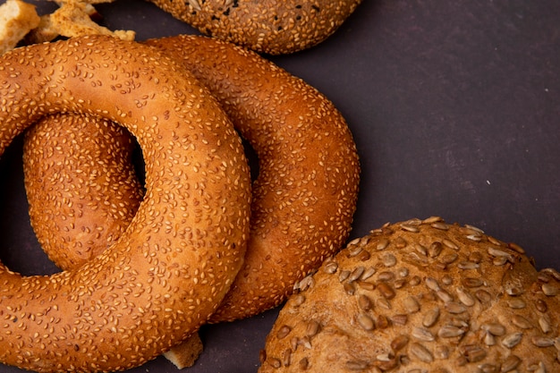 Vista do close-up de pães como bagel e espiga em fundo marrom com espaço de cópia