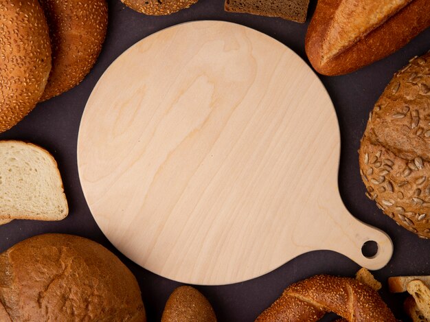Vista do close-up de tábua com pães ao redor como baguete de bagel de espiga no fundo marrom
