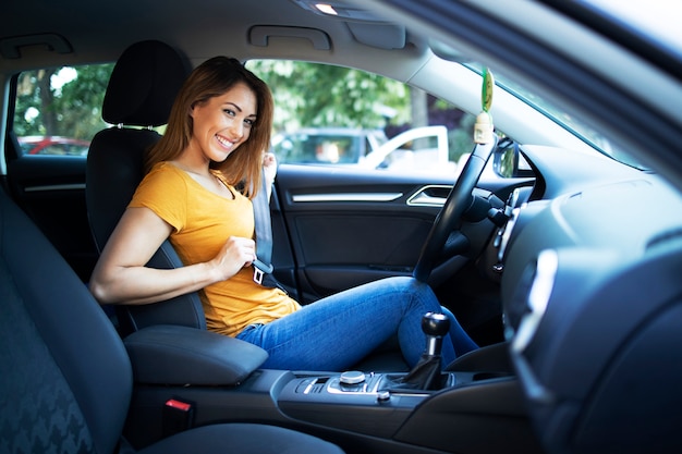 Vista do interior do carro de motorista feminina colocando o cinto de segurança