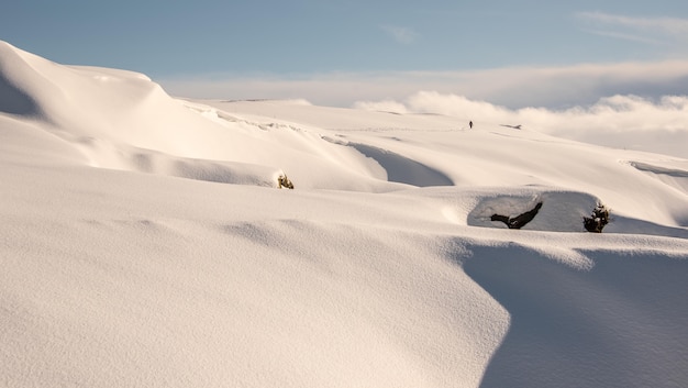 Vista do topo de uma montanha coberta de neve com um alpinista caminhando sozinho e um horizonte nublado