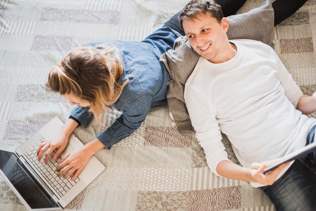 Vista elevada, de, um, par relaxando, cama, usando computador portátil, e, tabuleta