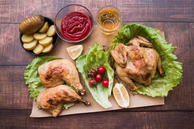 Vista elevada do frango assado para o jantar com cerveja; fatias de batata; limão e molho no papel marrom