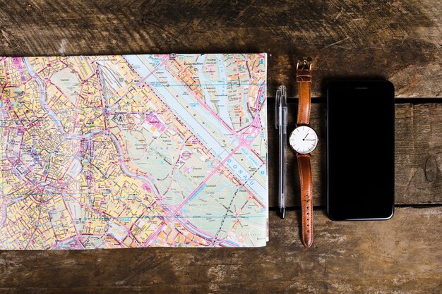 Vista elevada do smartphone, caneta, relógio de pulso, mapa em fundo de madeira