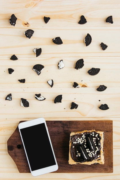 Foto grátis vista elevada do smartphone com pastelaria perto de pedaços de bolachas