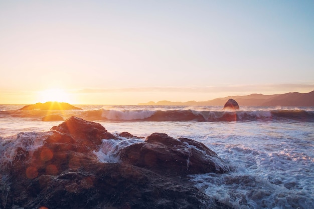 Vista fascinante das ondas do mar batendo nas rochas perto da costa durante o pôr do sol