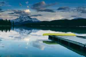 Foto grátis vista fascinante do cais perto do lago rodeado pela natureza exuberante e as montanhas