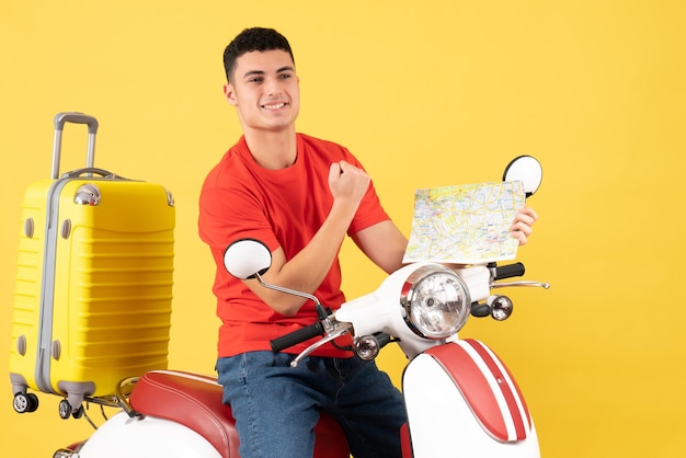 Vista frontal alegre homem bonito em uma motocicleta segurando o mapa